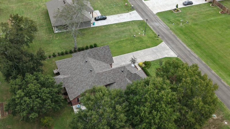 Drone view of a home with a new shingle roof on a corner lot shaded by trees