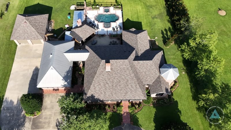 Drone view of a large hip roof replacement with a metal-roofed wing and pool behind