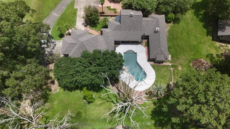 Straight-down drone view of a gray shingle roof beside a curved pool and lush yard