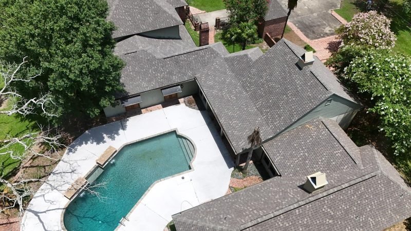 Drone close-up of gray shingle roof sections, valleys and vents above a backyard pool