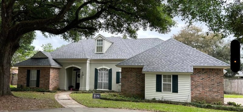 Acadian-style home with brick and white siding and a new light gray roof under a spreading oak