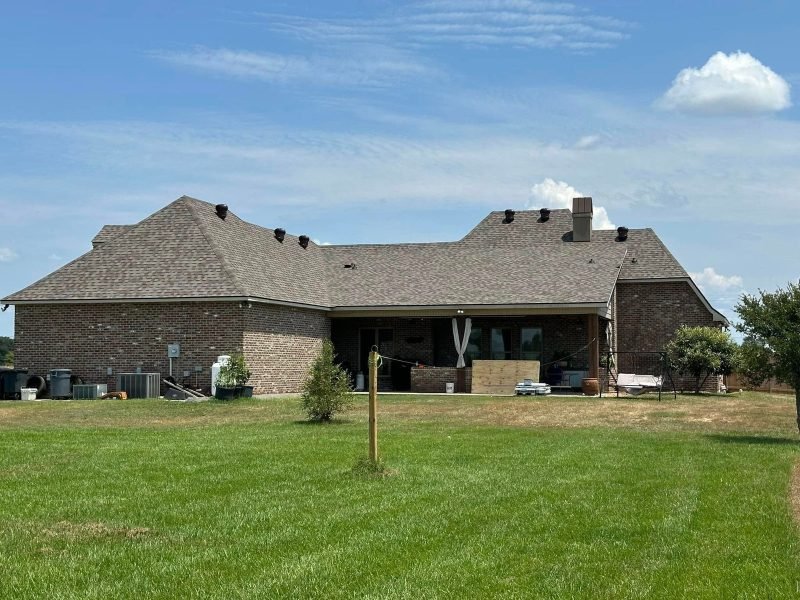 Back of a brick home with a new brown hip roof and covered porch across a lawn
