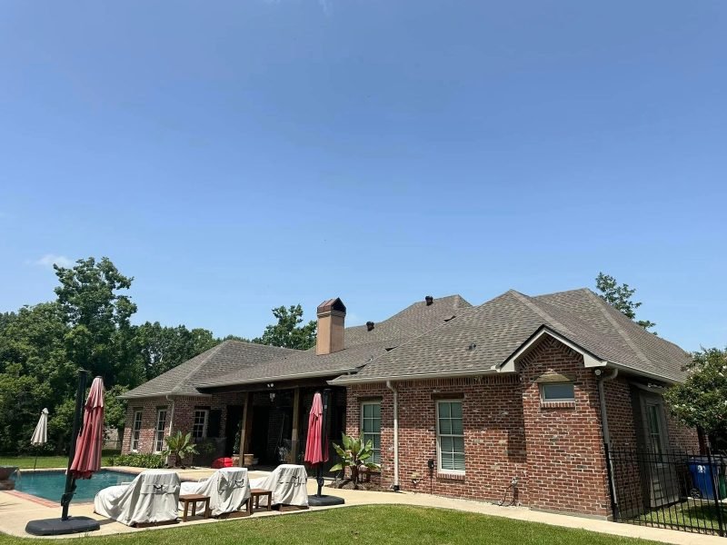 Brick home with a new brown roof and chimney, seen from the pool deck