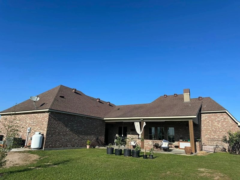 Back of a brick home with a new brown shingle roof over a covered patio