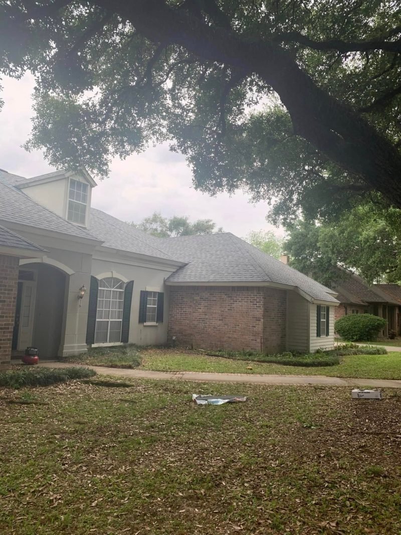 Brick and stucco home with a new gray roof and dormer under heavy live oak branches