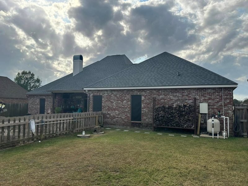 Back of a brick home with a new dark gray roof and chimney, wooden fence in front