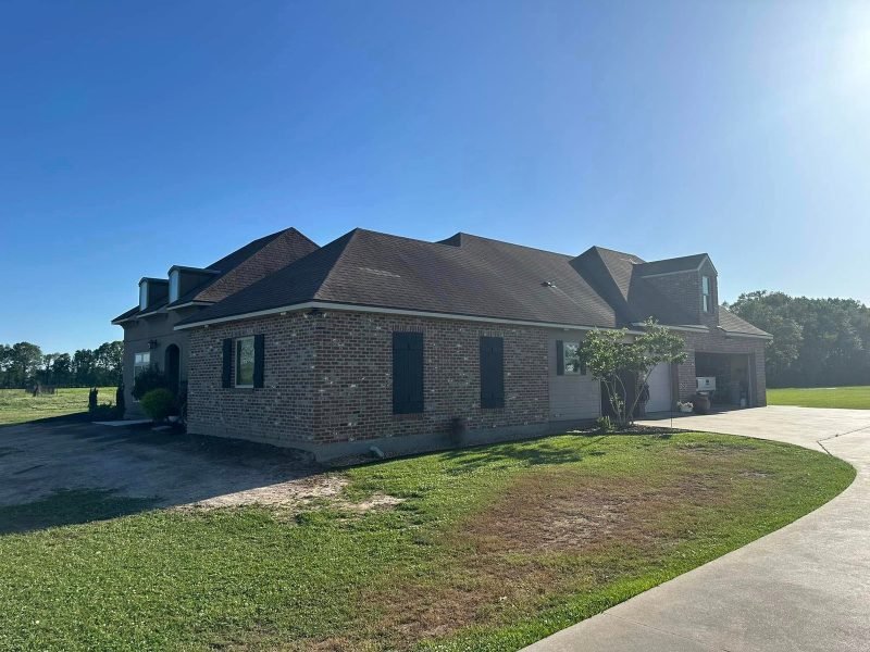 Brick home with a new dark brown roof and dormers beside a curved driveway