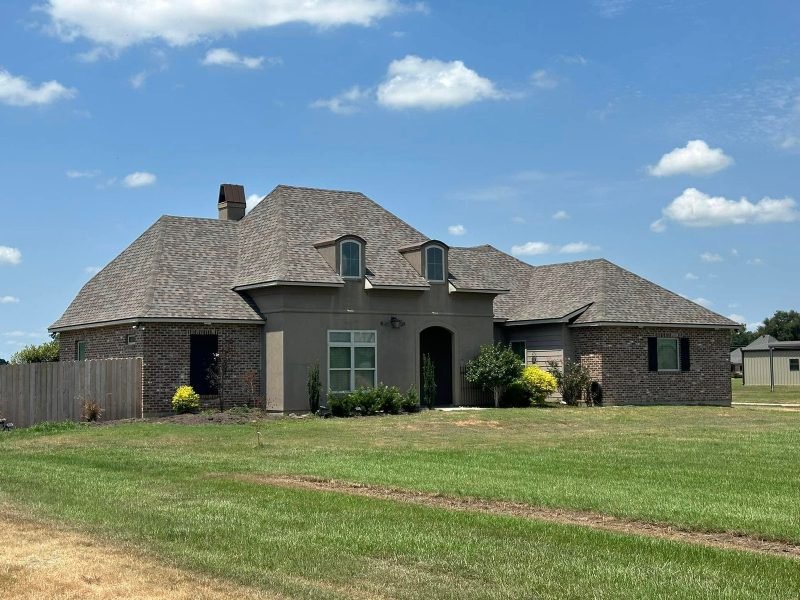 Brick and stucco home with two dormers and a new brown shingle roof