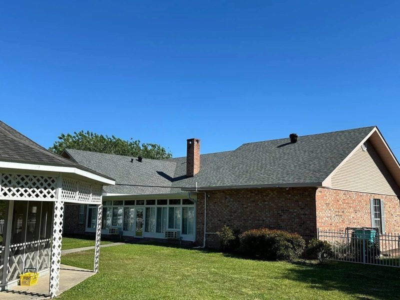 Brick home with a new gray roof, chimney and a white lattice porch on a sunny day