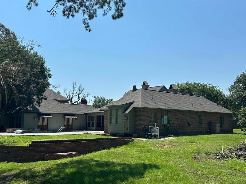 Brick home and wing with new shingle roofs above a low brick retaining wall