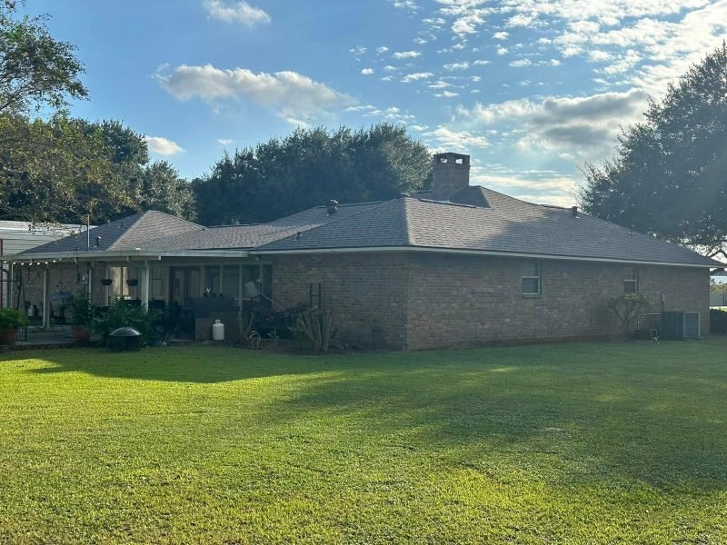 Brick home with a new gray hip roof, chimney and screened porch in afternoon light