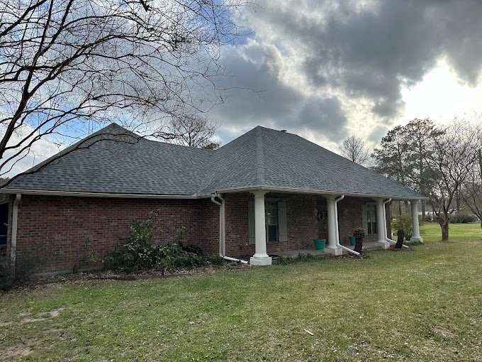 Brick ranch home with a new gray shingle roof and white porch columns under a cloudy sky