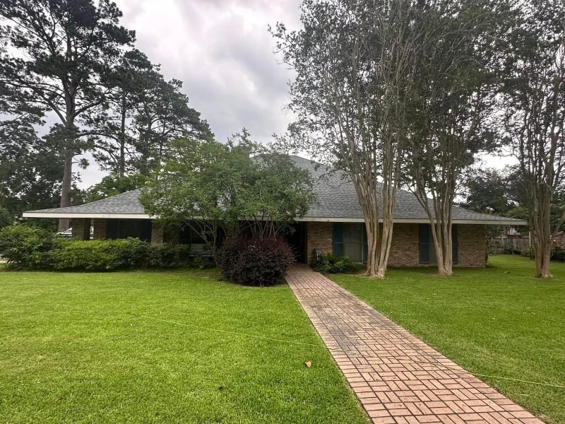 Brick walkway leading to a ranch home with a new gray roof under crepe myrtles