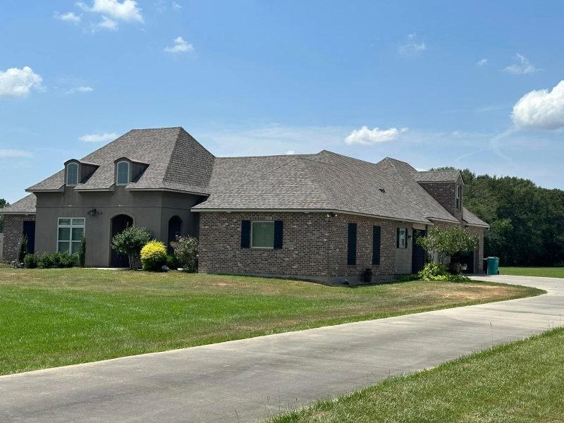 French-style brick home with dormers and a new hip roof, seen along the driveway