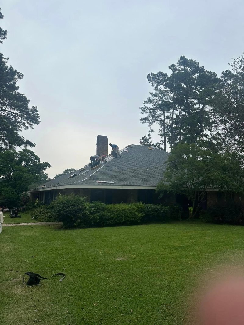 Low single-story home with a new gray roof and chimney seen through trees