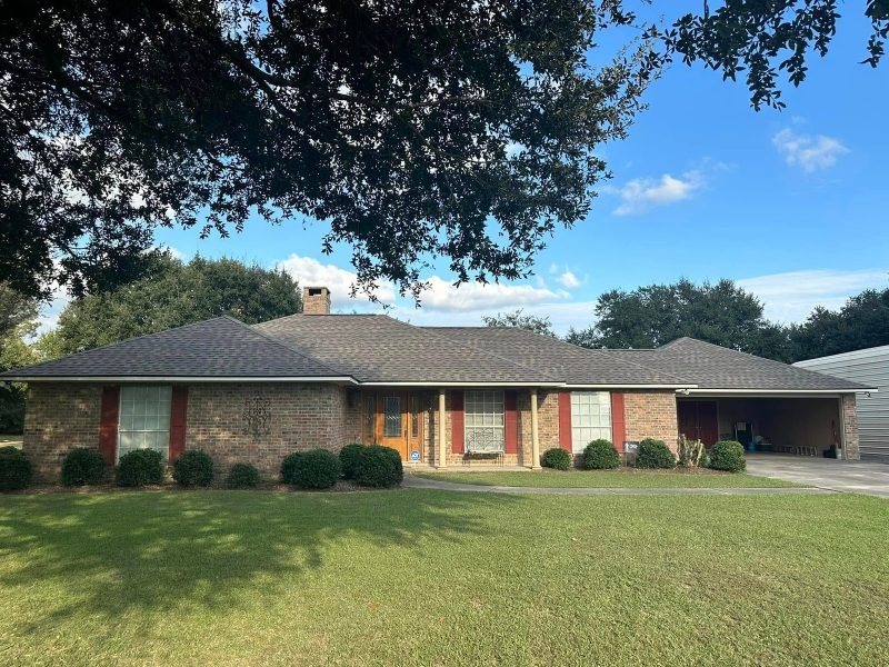 Long brick ranch home with a new gray roof, red shutters and an oak branch overhead