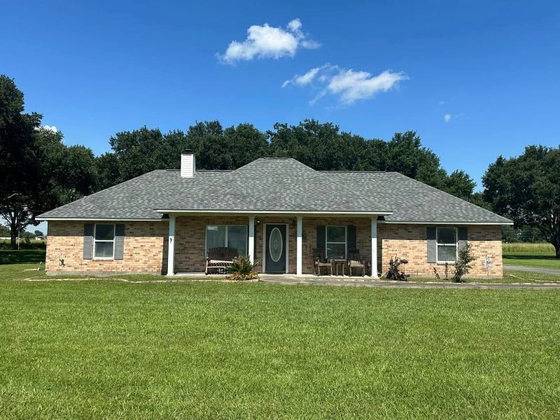 Brick ranch home with a new gray roof and a covered front porch, oaks behind