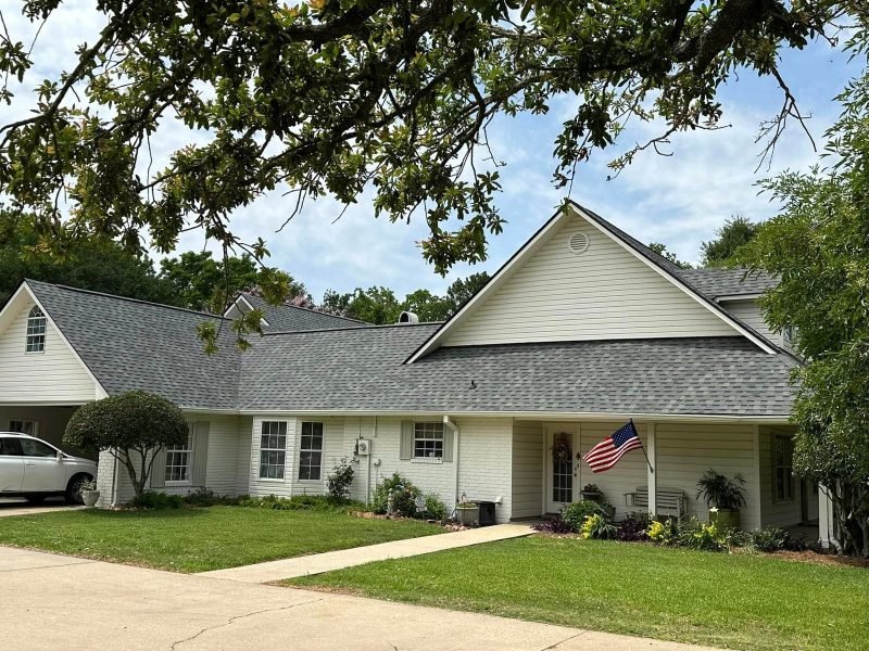 Two-story home with light siding, a front gable and a new gray roof, flag on the porch
