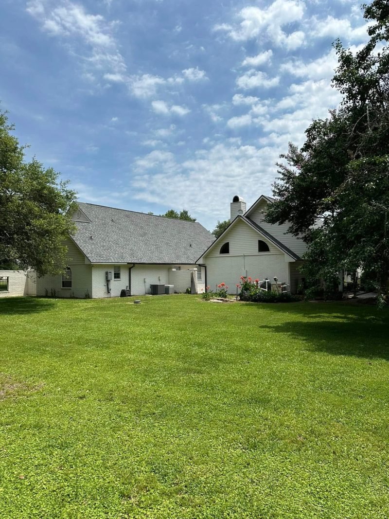 White home and side wing with new gray shingle roofs set in a wide lawn