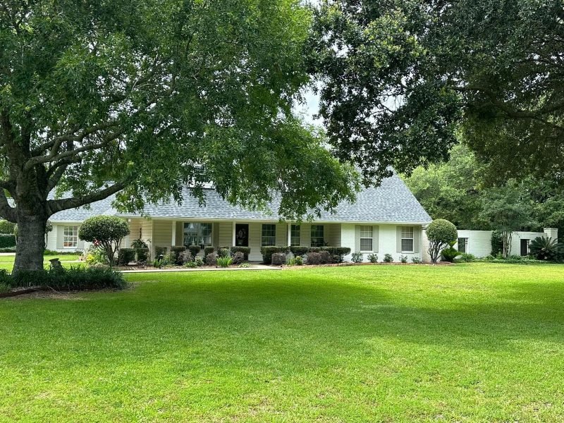 White single-story home with a new gray roof seen across a lawn under large oak trees