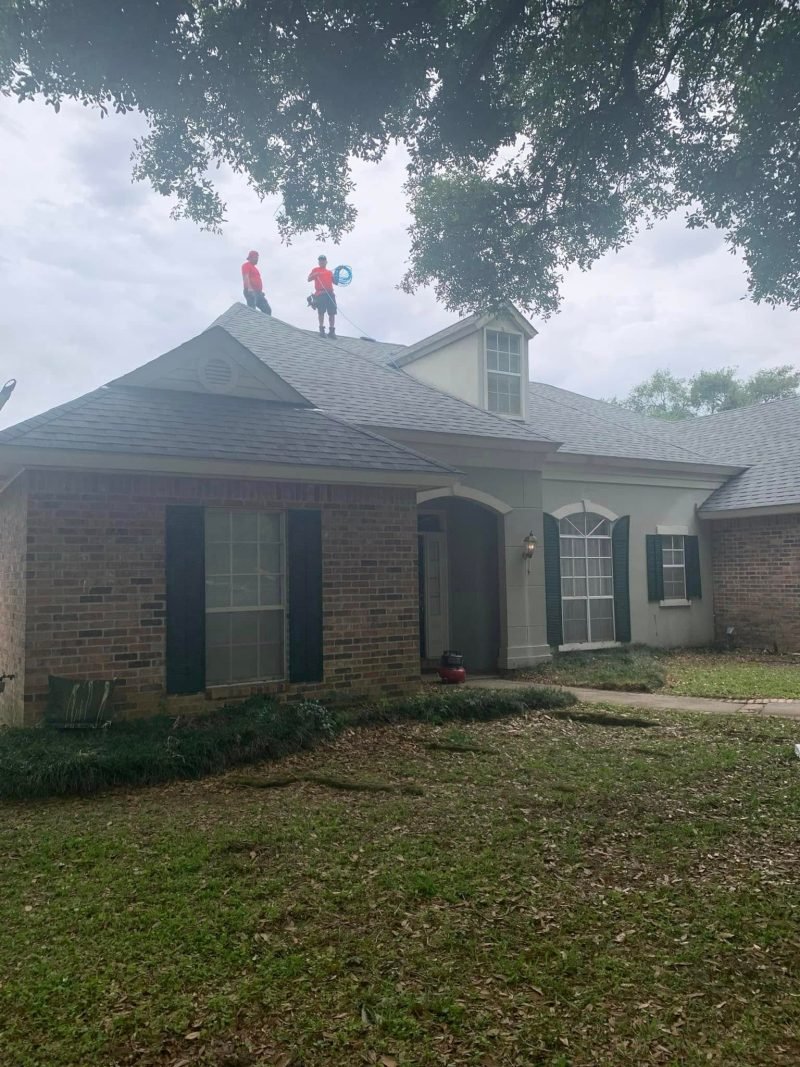 Two roofers working on the ridge of a brick home during a re-roof