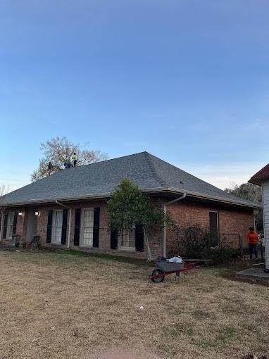 Brick ranch home with a new gray roof, a wheelbarrow and crew member in the yard