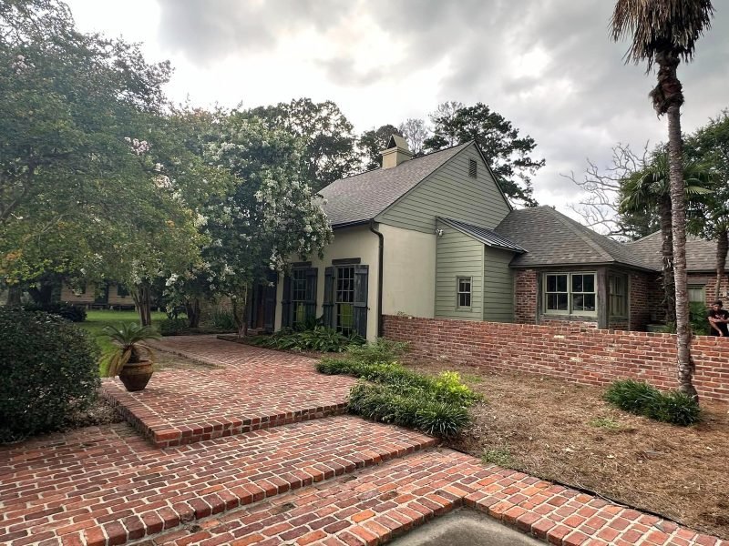 Green-sided home with a new gray roof above brick steps and planters