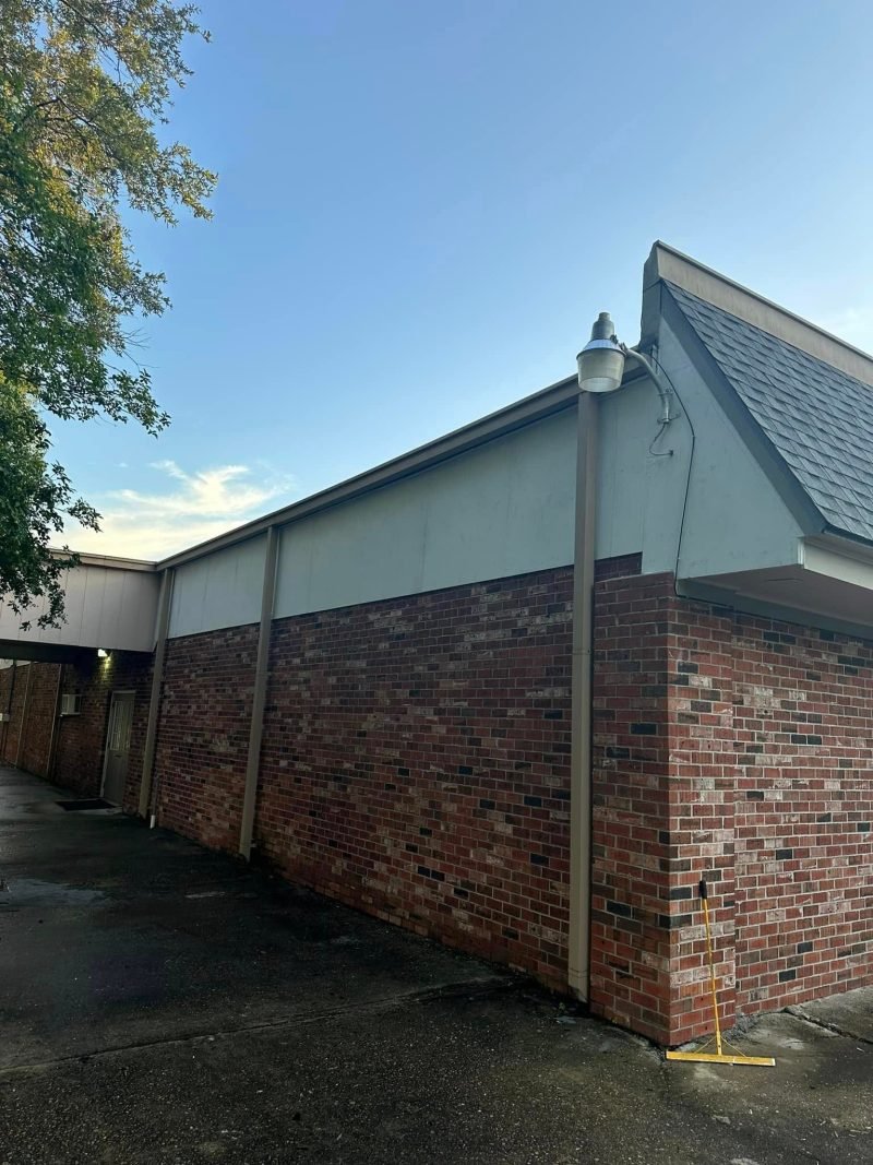 Brick wall and painted gable trim under a new shingle roof edge
